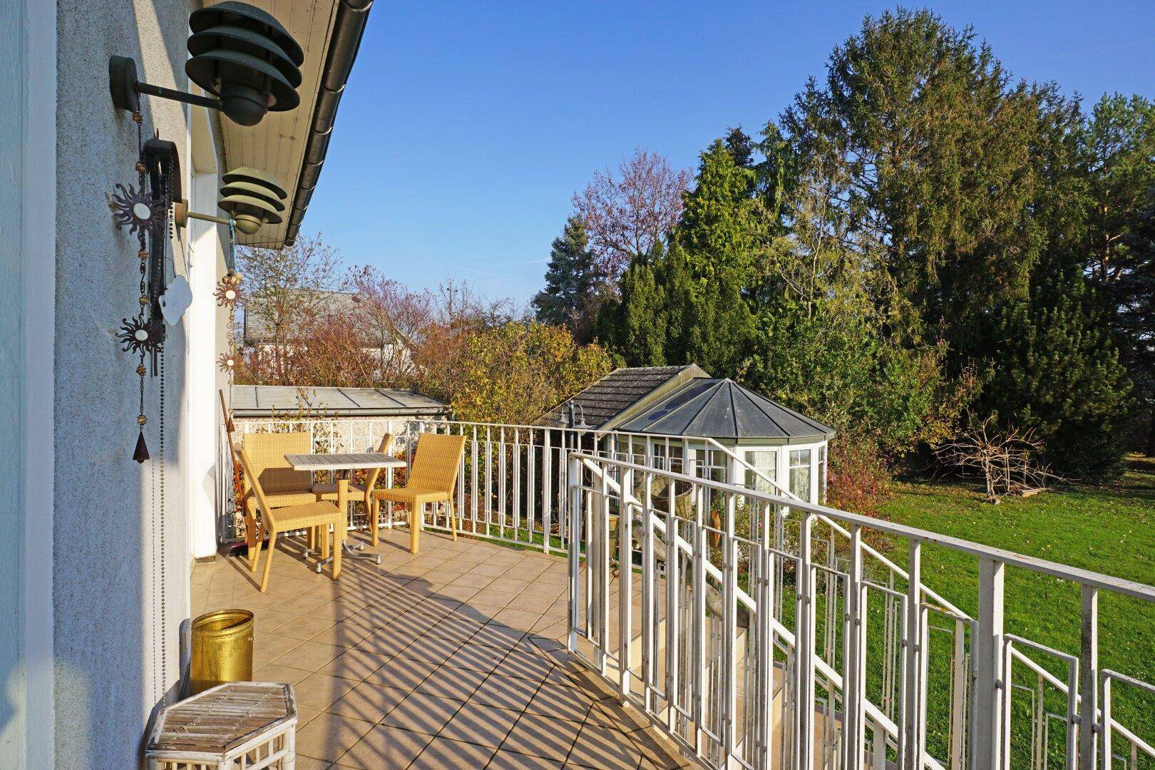 Sonniger Balkon mit Fliesenboden und Sitzgelegenheiten, mit Blick in den Garten.