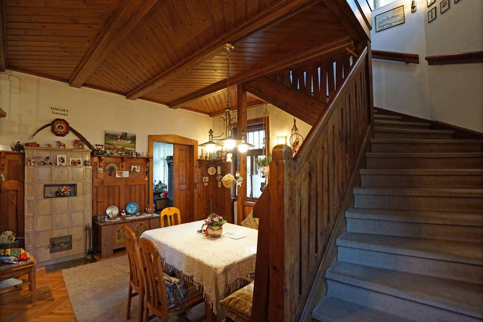 Rustikaler Essbereich mit Holzbalkendecke, Holztisch und einer Holztreppe.