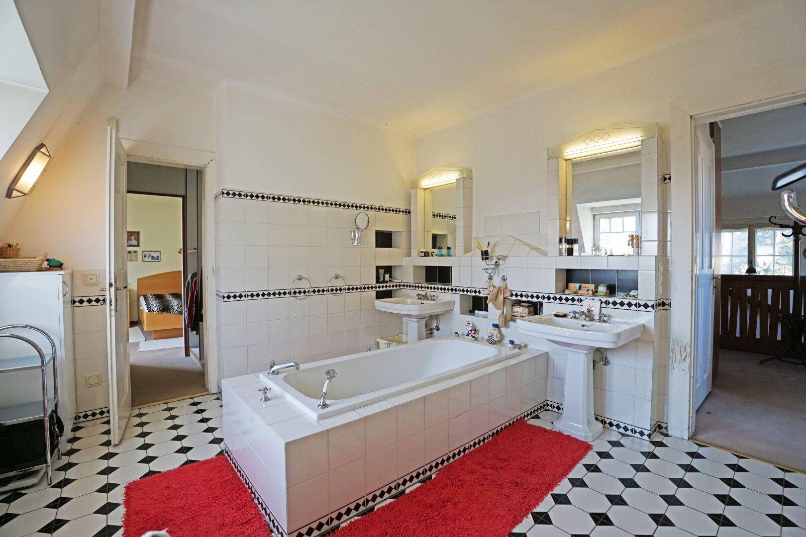 Geräumiges Badezimmer mit Badewanne, Doppelwaschbecken und schwarz-weißem Fliesenmuster.