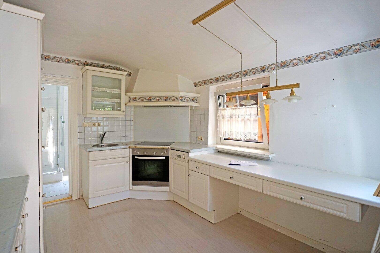 Küche mit weißen Einbauschränken, integriertem Backofen und einem Fenster mit Blick nach draußen.