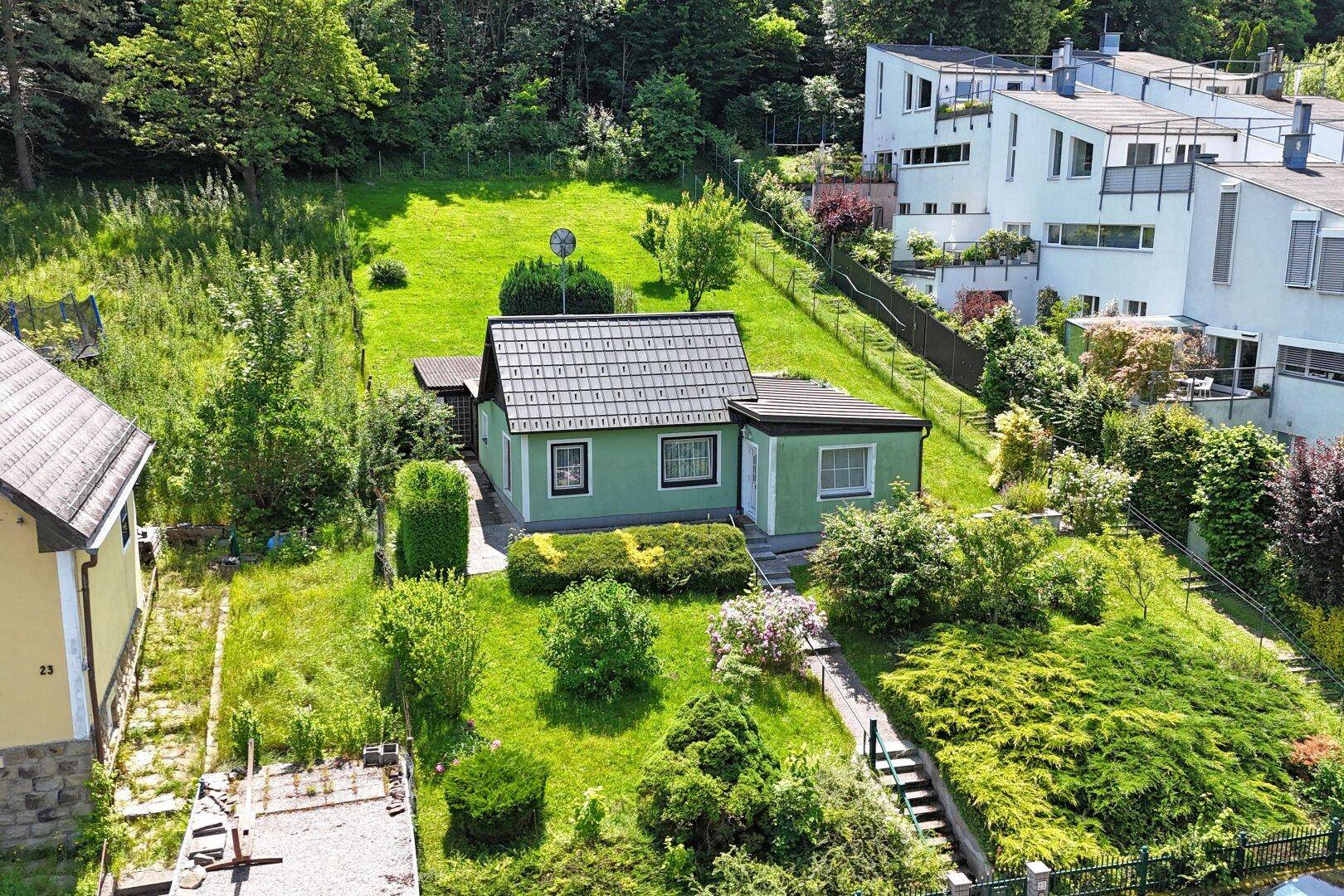 Luftaufnahme des hellgrünen Hauses mit Garten und angrenzenden modernen Wohngebäuden in der Umgebung.