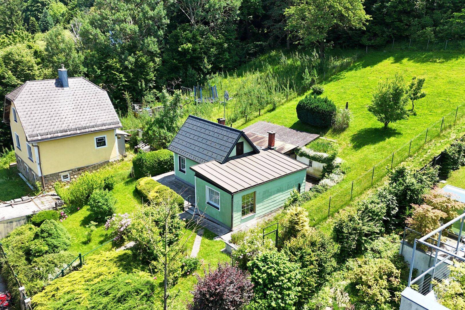 Luftaufnahme eines Grundstücks mit einem grünen Haus, umgeben von weitläufigen Rasenflächen und Bäumen.