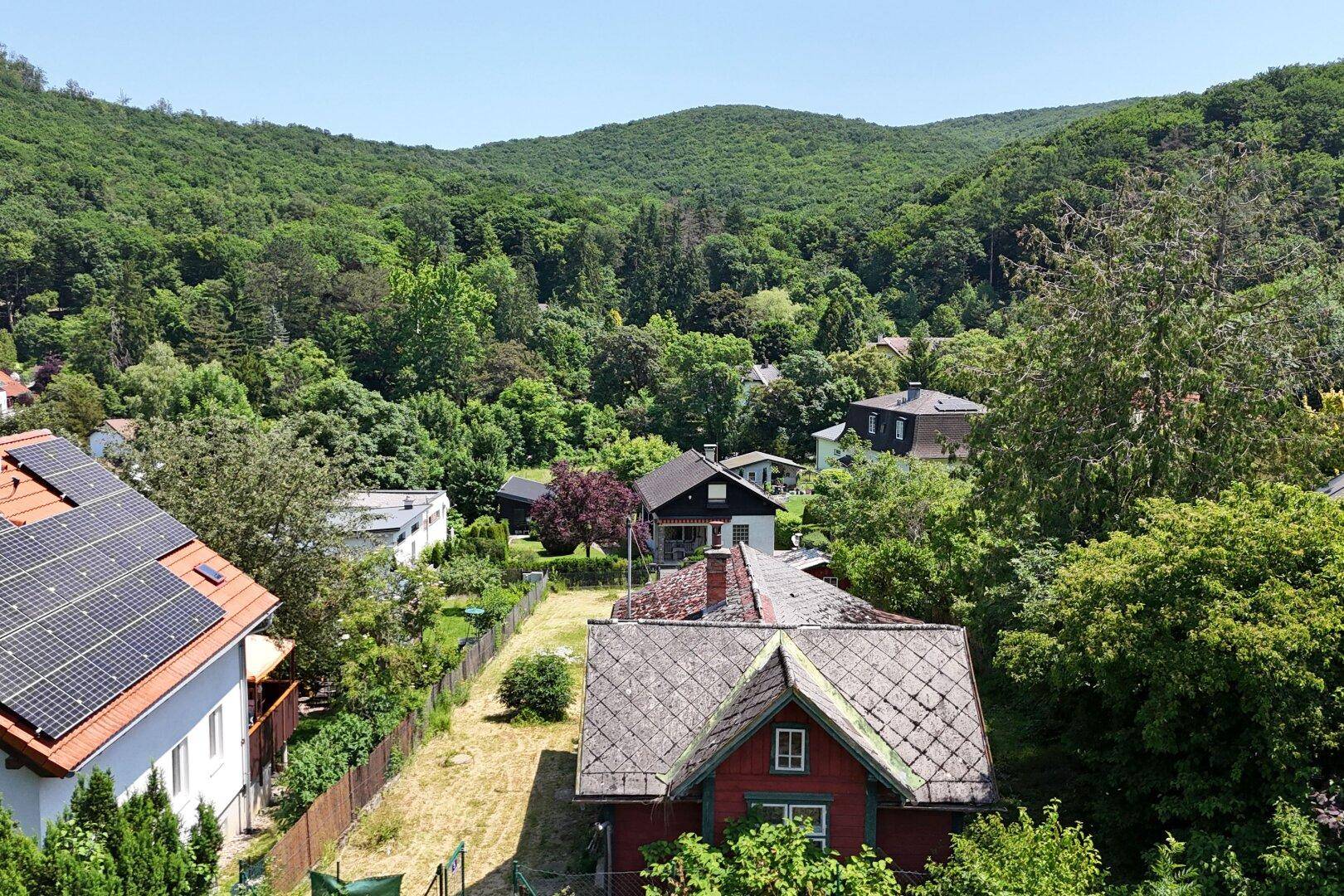 Panoramablick auf eine Wohnsiedlung mit Häusern, umgeben von dichten grünen Hügeln und Wäldern.