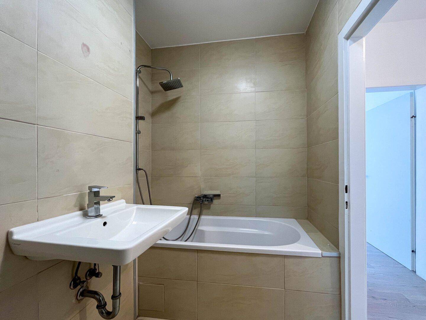 Gefliestes Badezimmer mit Badewanne, Duschvorrichtung und Einzelwaschbecken.