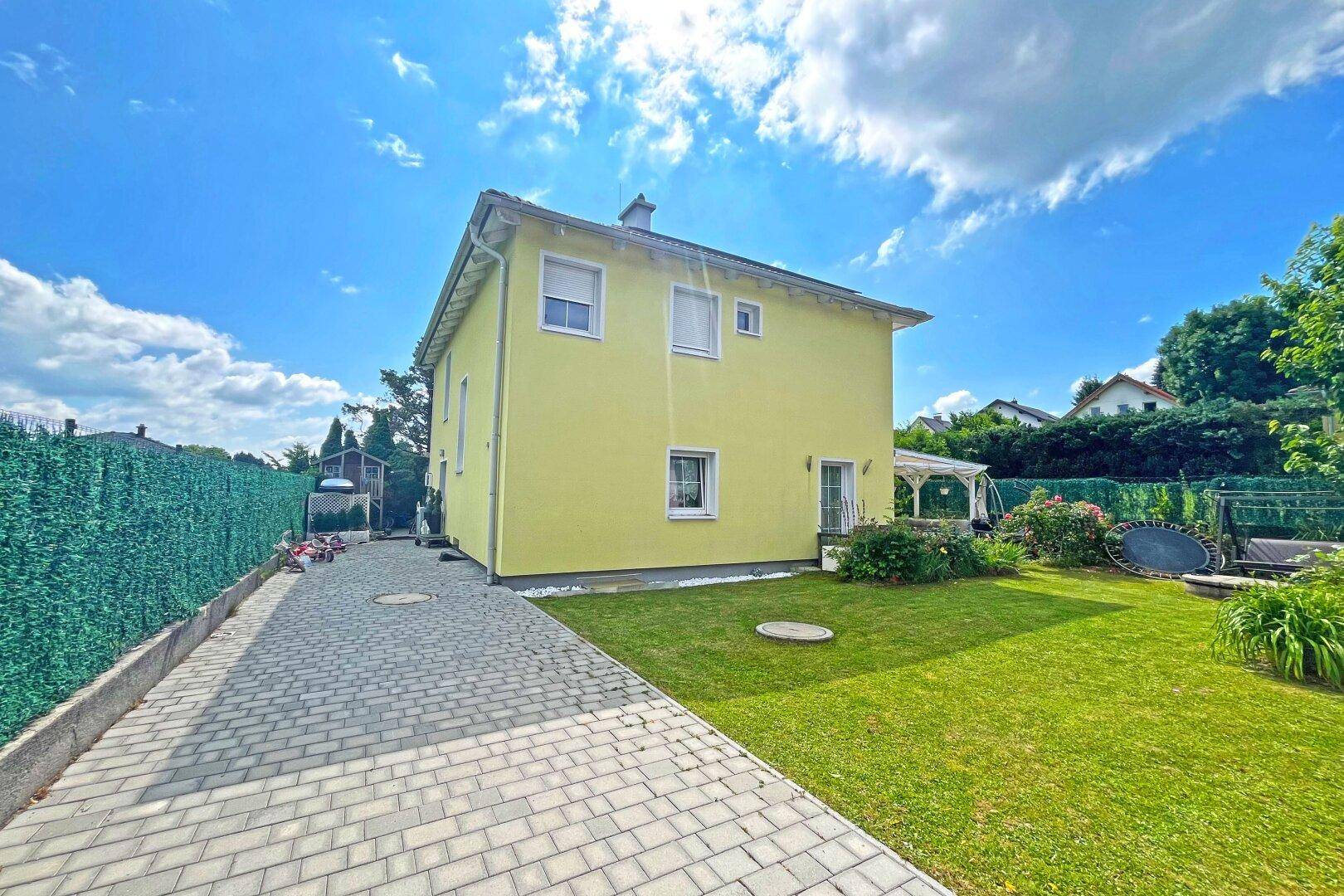 Seitenansicht des gelben Hauses mit gepflasterter Zufahrt und gepflegtem Rasen im Gartenbereich.
