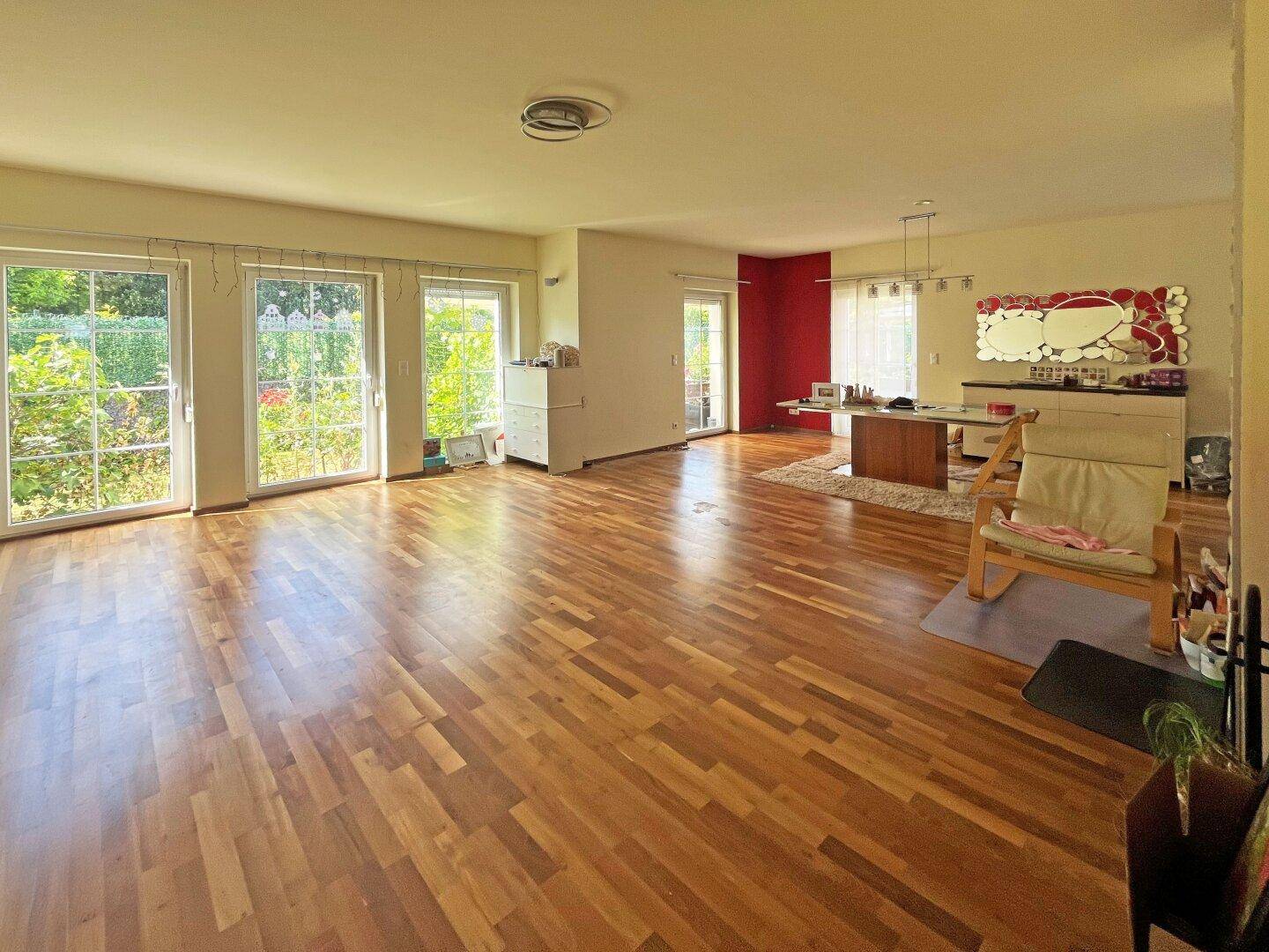 Großzügiges Wohnzimmer mit Holzboden, großen Fenstern und Zugang zum Gartenbereich.