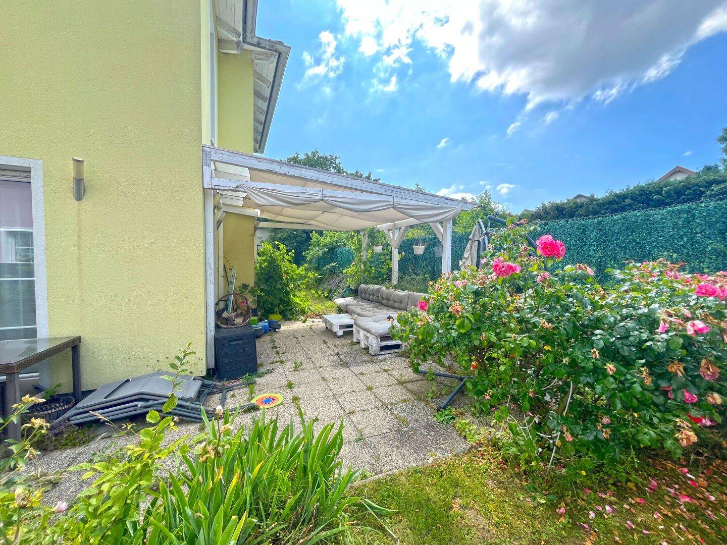 Überdachte Terrasse mit Sitzgelegenheiten und Rosenbüschen, ideal für entspannte Stunden im Freien.