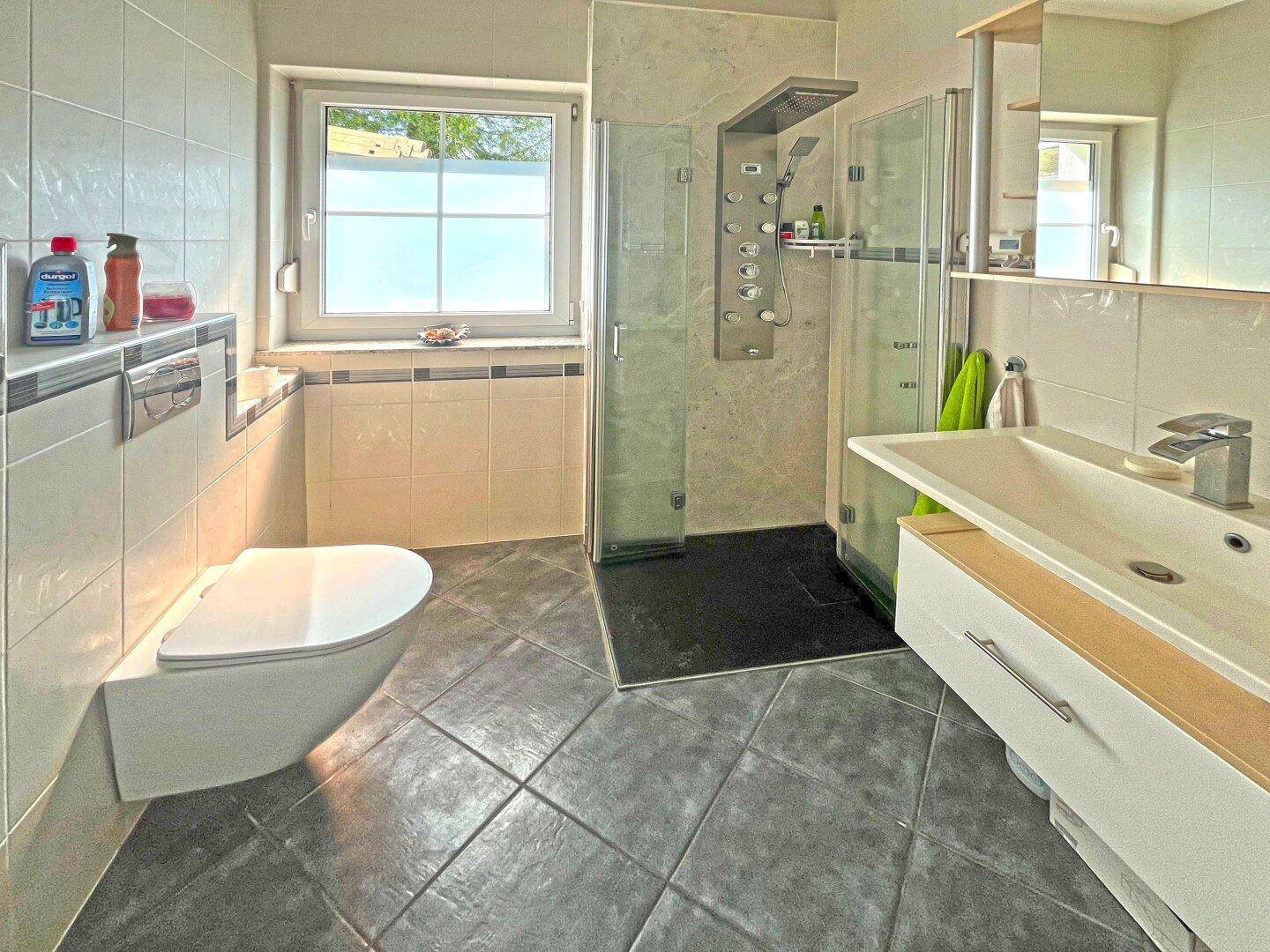 Modernes Badezimmer mit Dusche, wandhängendem WC und Fenster für Tageslicht.