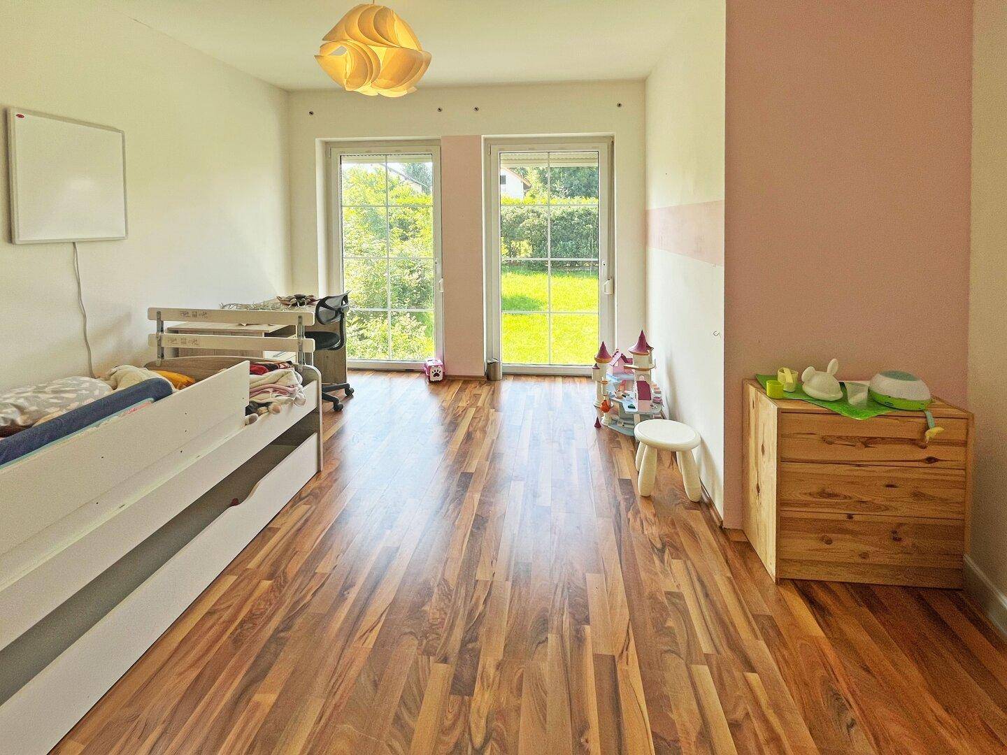 Kinderzimmer mit Holzboden, großen Fenstern und Blick ins Grüne, ideal für kleine Bewohner.