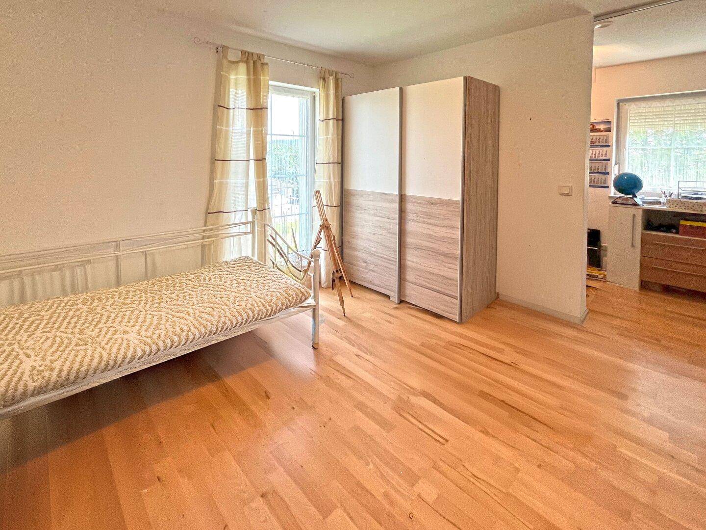 Gemütliches Schlafzimmer mit Holzboden, Kleiderschrank und Vorhängen am Fenster.