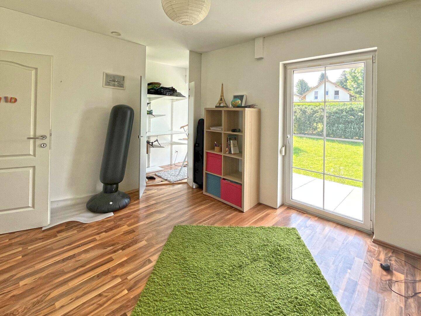 Heller Raum mit Holzboden, grünem Teppich und direktem Zugang zum Gartenbereich.
