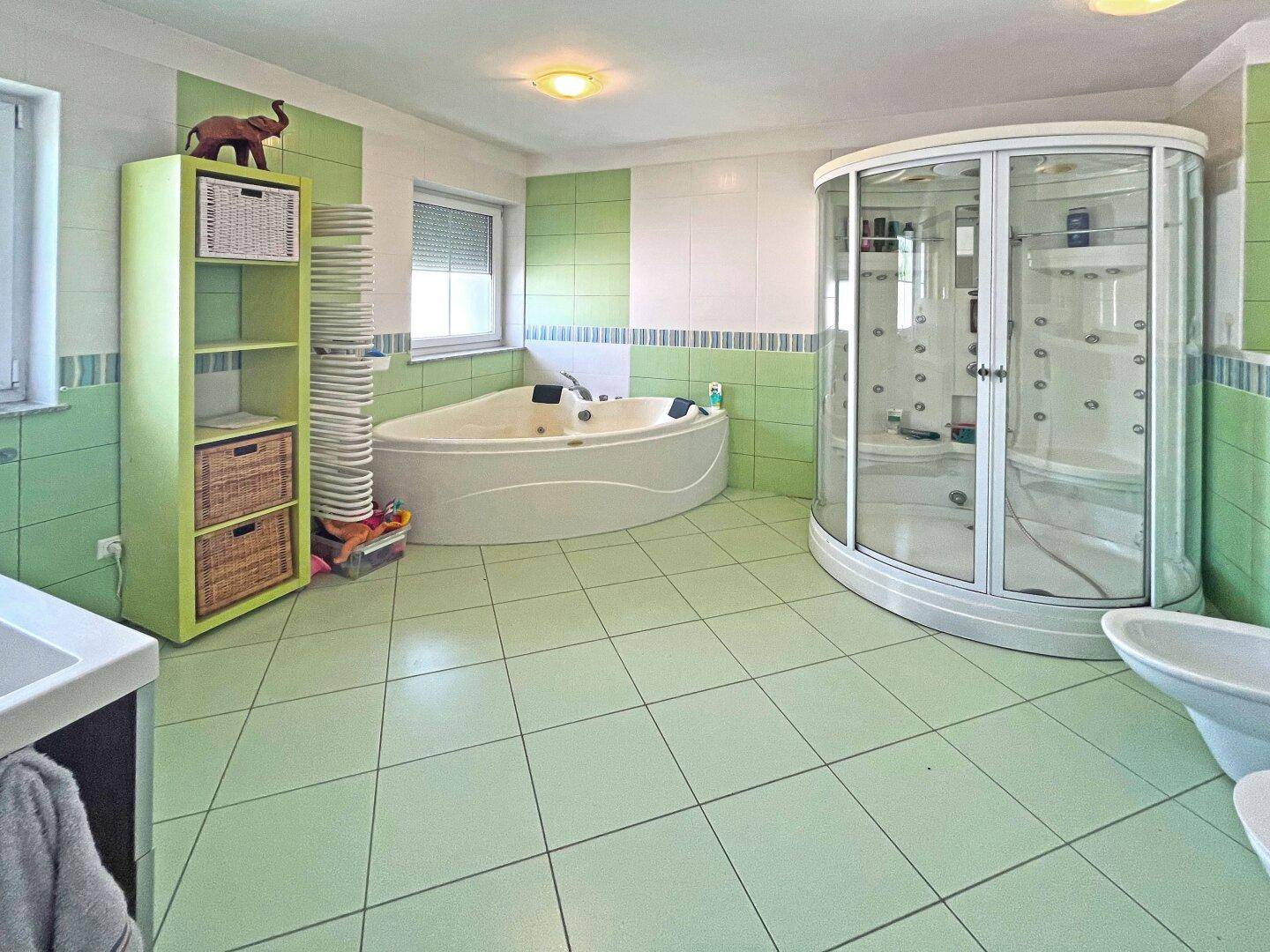 Geräumiges Badezimmer mit Eckbadewanne, Duschkabine und grünen Fliesen, bietet viel Platz.