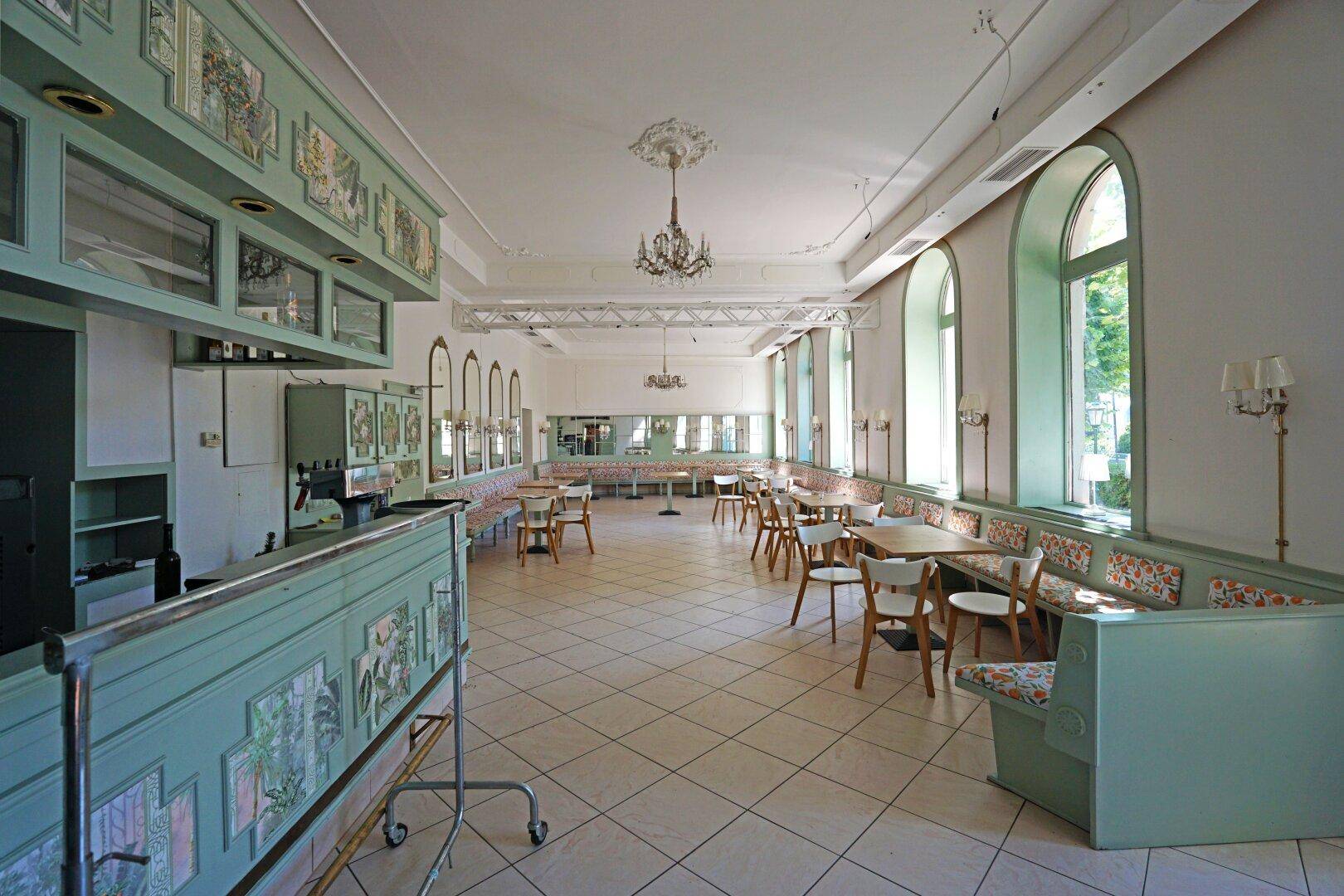 Geräumiger Speisesaal mit hellgrünen Bänken, Holztischen und großen Rundbogenfenstern.
