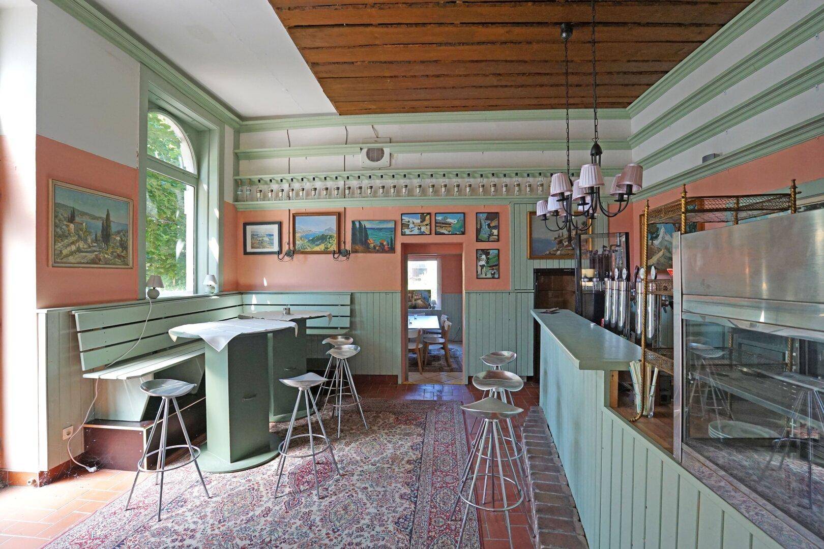 Bar-Bereich mit Holzbalkendecke, hohen Hockern und farbigen Wänden in Grün und Orange.