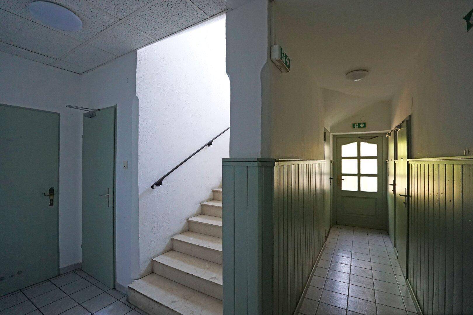 Treppenhaus und Flur mit hellgrünen Holzvertäfelungen und Fliesenboden.