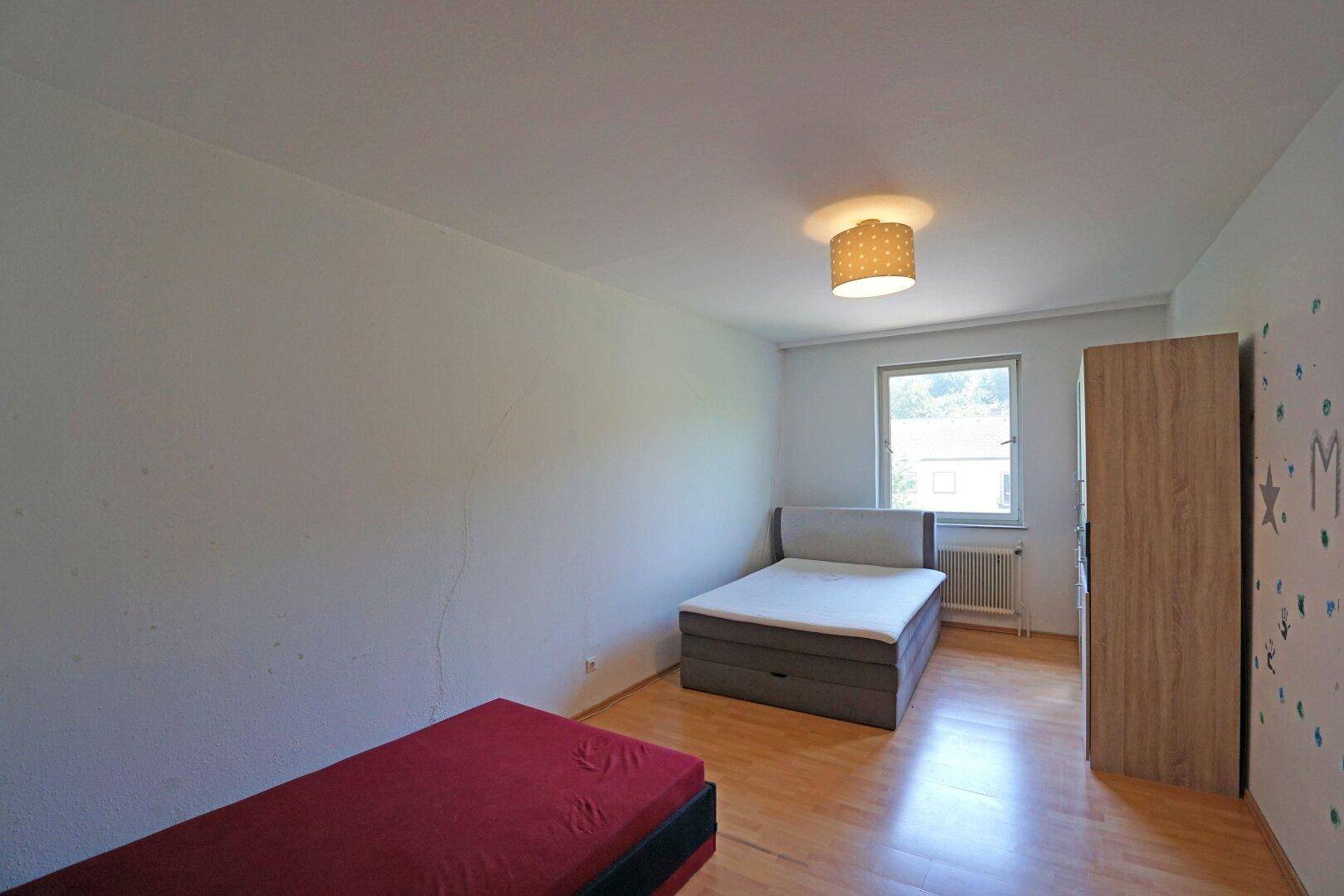 Schlafzimmer mit zwei Betten, Holzfußboden und einem Fenster mit Blick ins Grüne.