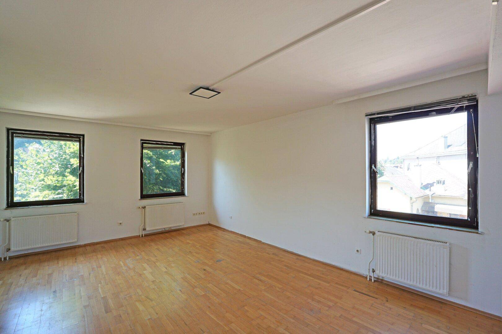 Geräumiges Zimmer mit Holzfußboden, drei Fenstern und Blick auf die Umgebung.