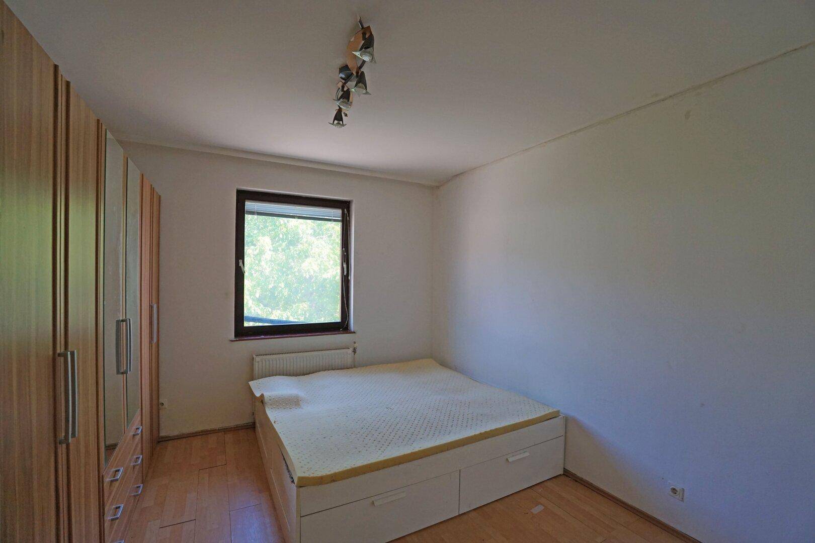 Schlafzimmer mit Bett, großem Kleiderschrank und Fenster mit Blick ins Grüne.