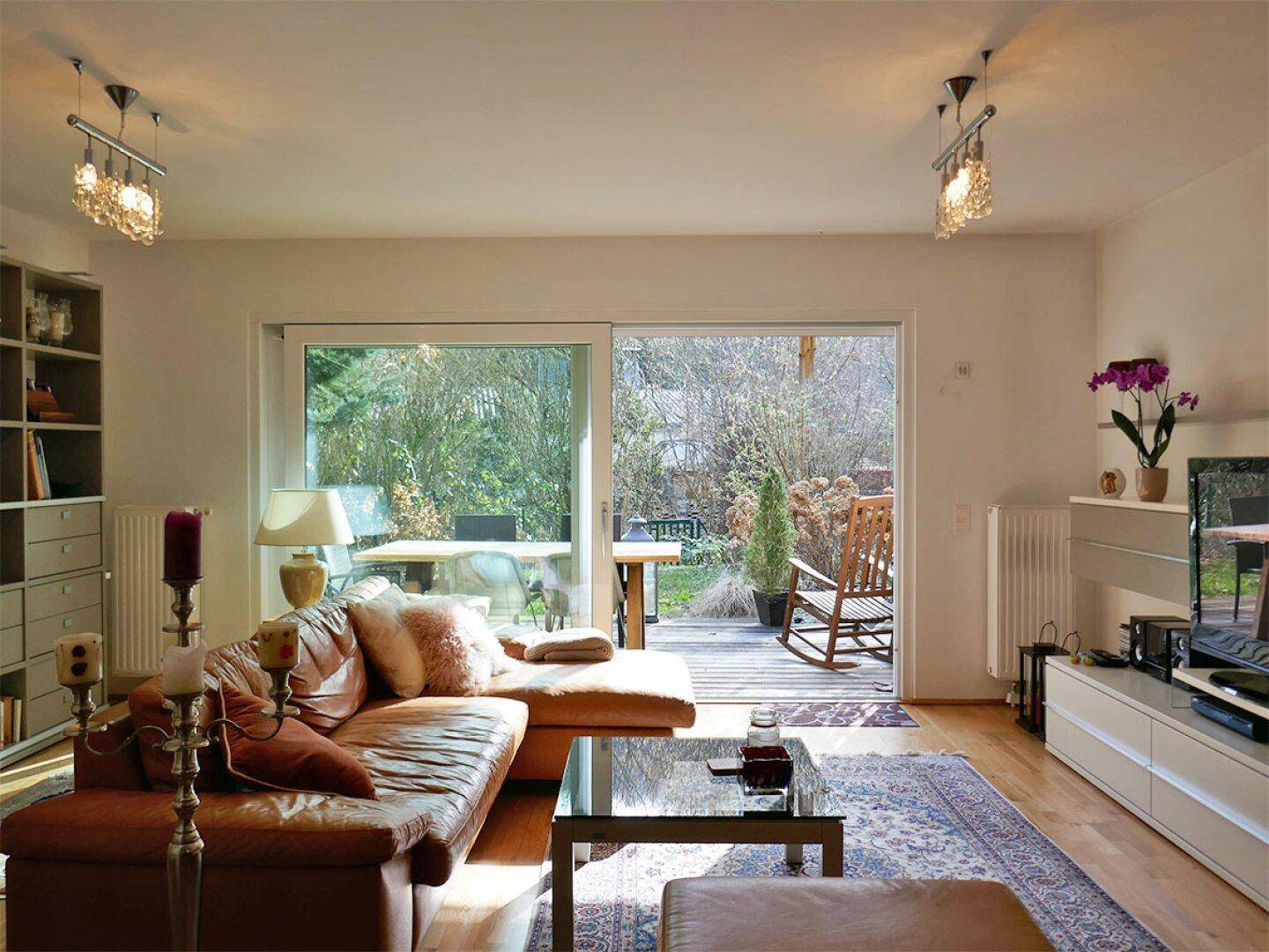 Gemütliches Wohnzimmer mit Ledersofa, Holzboden und großer Schiebetür, die zur Terrasse führt.