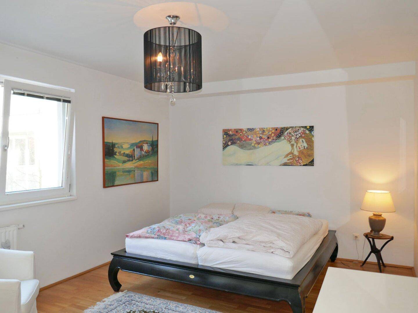 Helles Schlafzimmer mit Holzboden, Doppelbett und modernen Kunstwerken an den Wänden.