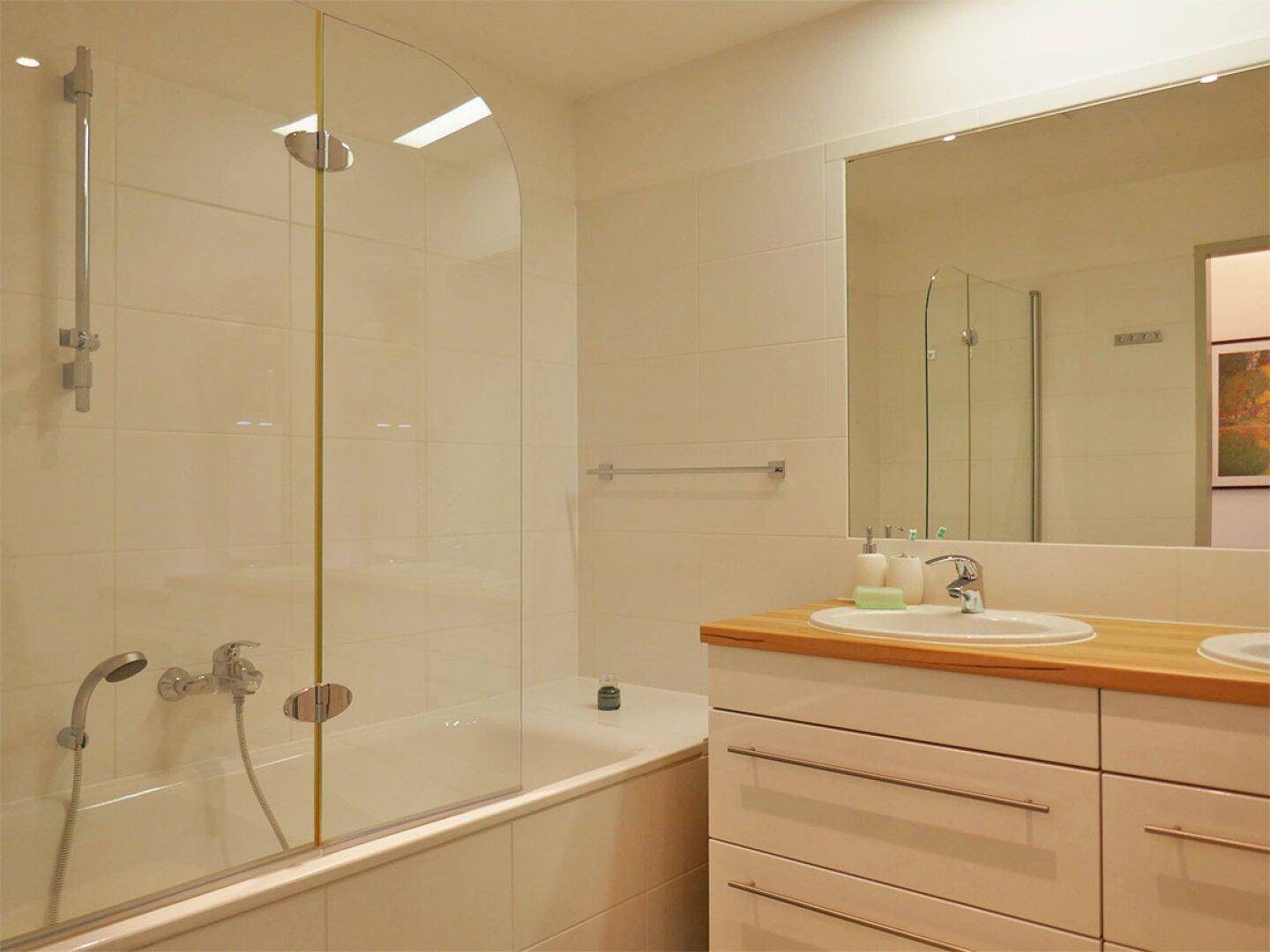 Modernes Badezimmer mit Badewanne, Duschabtrennung und Doppelwaschbecken mit Holzplatte.