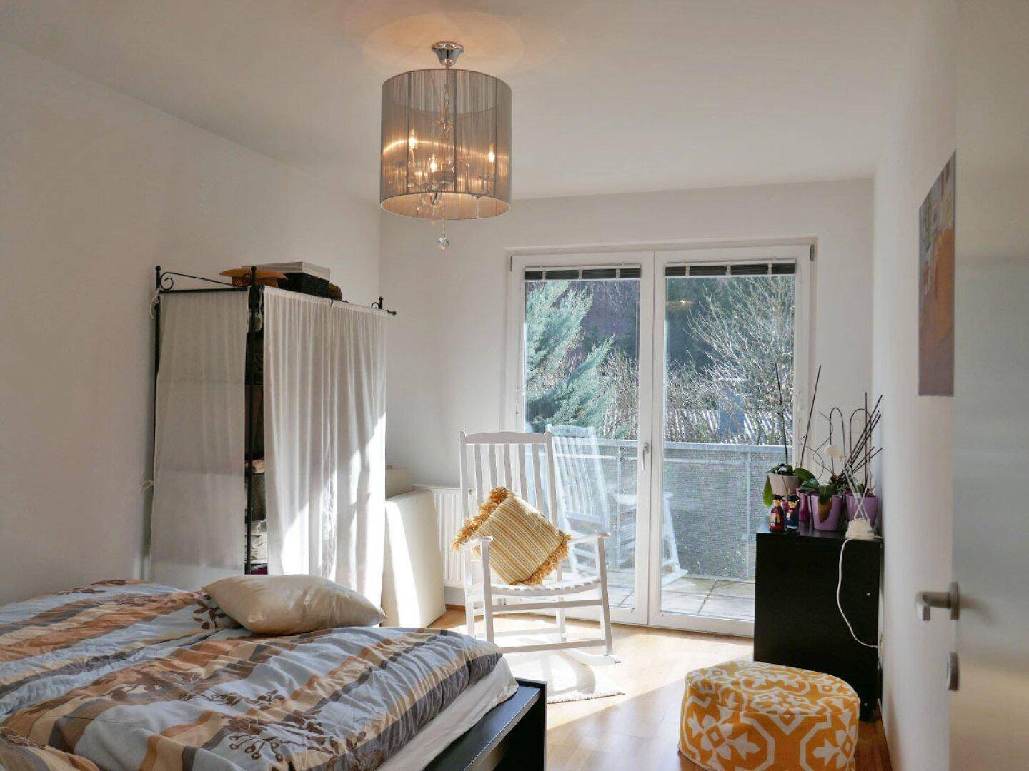 Gemütliches Schlafzimmer mit Holzboden, Bett und Zugang zu einem sonnigen Balkon.