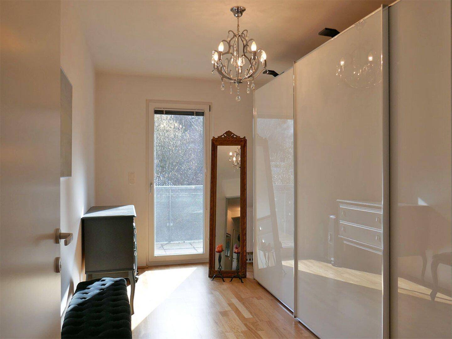 Heller Raum mit Spiegelschrank, Holzboden und Zugang zu einem kleinen Balkon.