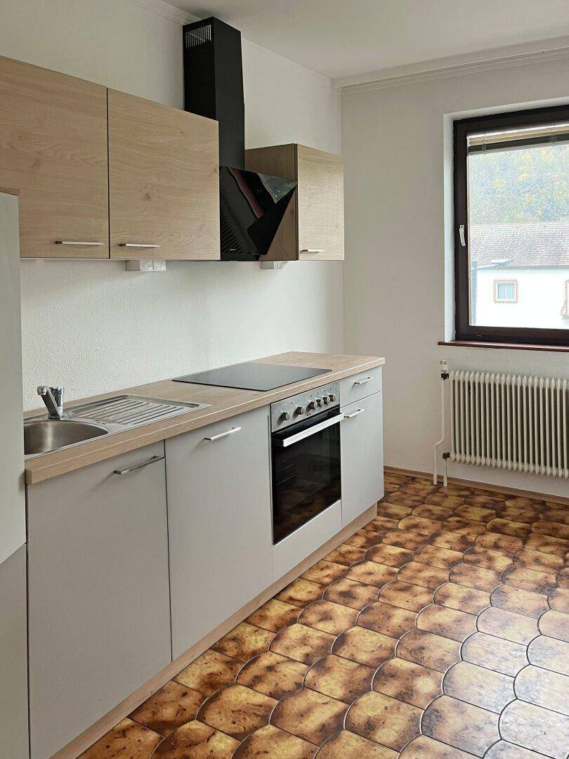 Moderne Küche mit hellgrauen und holzfarbenen Schränken, Backofen und Dunstabzugshaube.