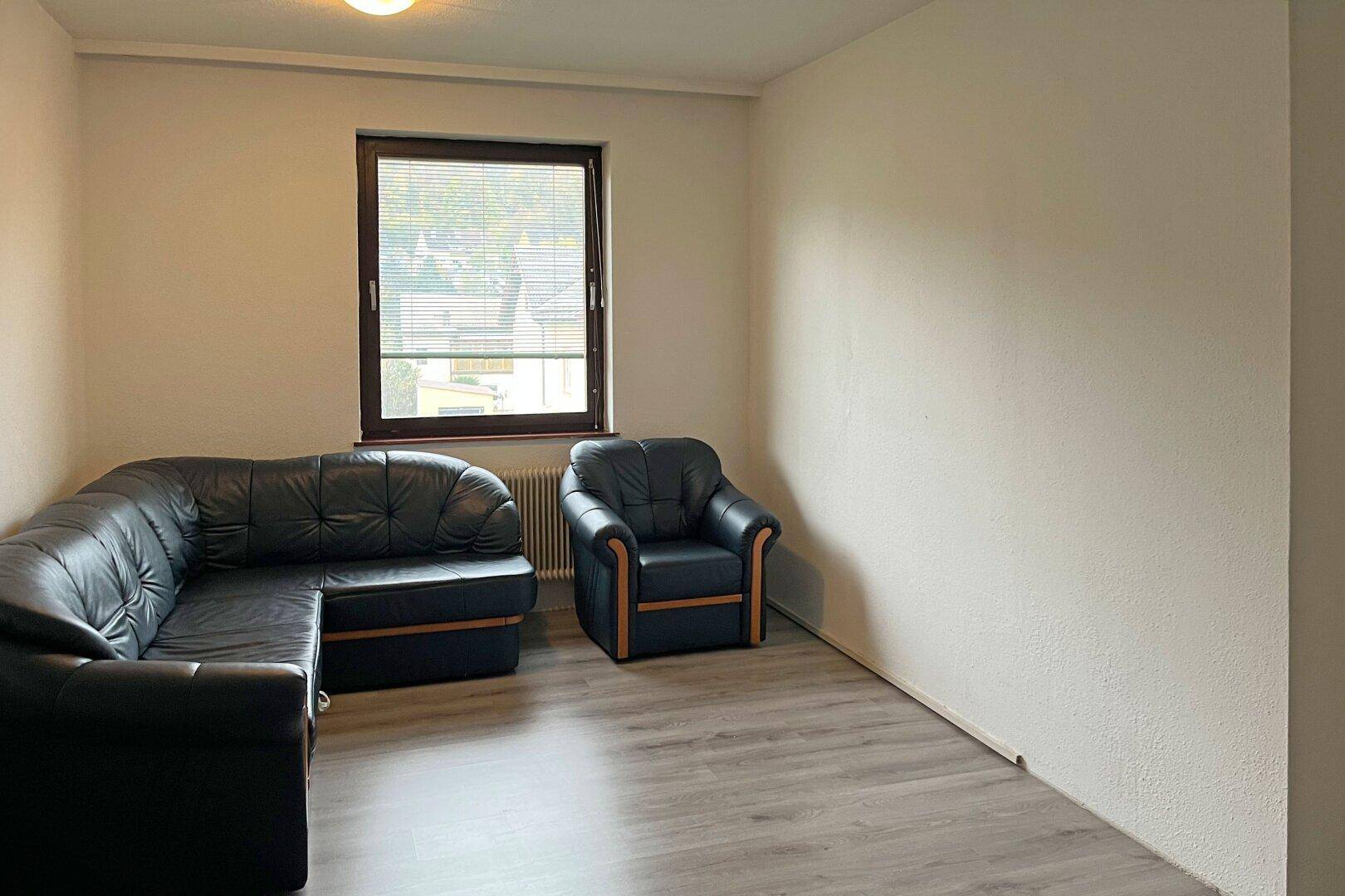 Wohnzimmer mit dunklem Ledersofa, Sessel und hellem Laminatboden.