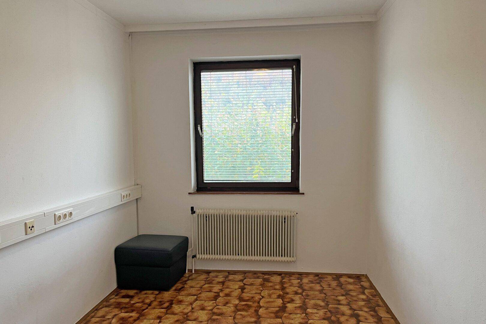 Kleines Zimmer mit Fenster, Heizkörper und gemustertem Fliesenboden.