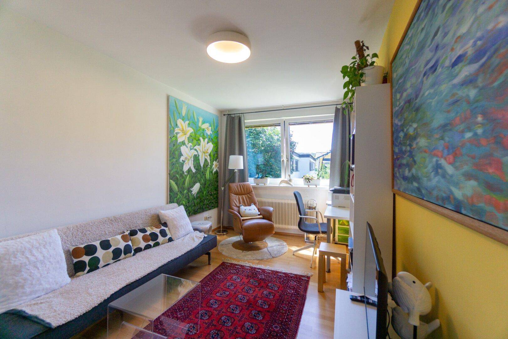 Gemütliches Wohnzimmer mit Sofa, Schreibtisch und Blick ins Grüne.