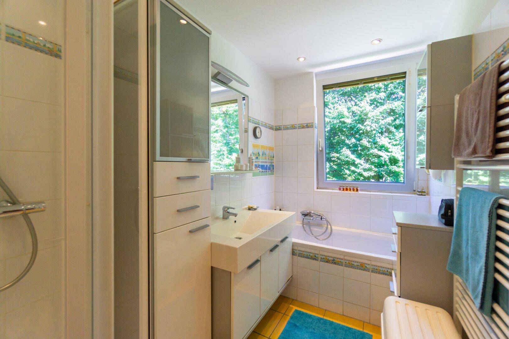 Helles Badezimmer mit Badewanne, Dusche und Fenster zum Garten.