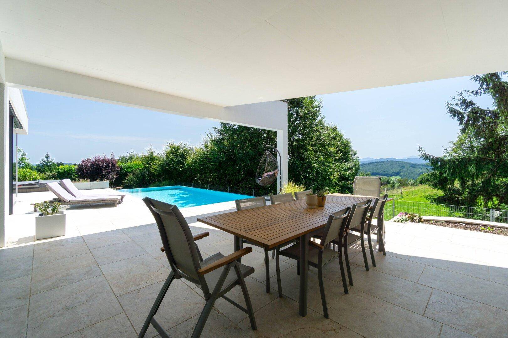 Große überdachte Terrasse mit Esstisch, Stühlen und weitem Blick über die Landschaft und den Pool.