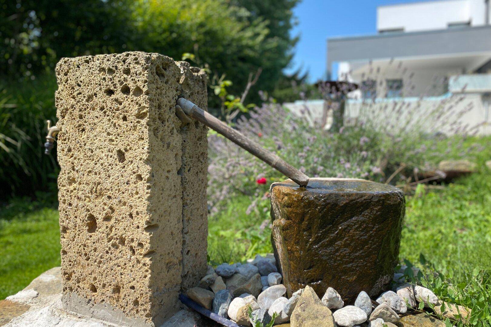 Detailaufnahme eines rustikalen Zierbrunnens aus Stein im gepflegten Gartenbereich der Villa.