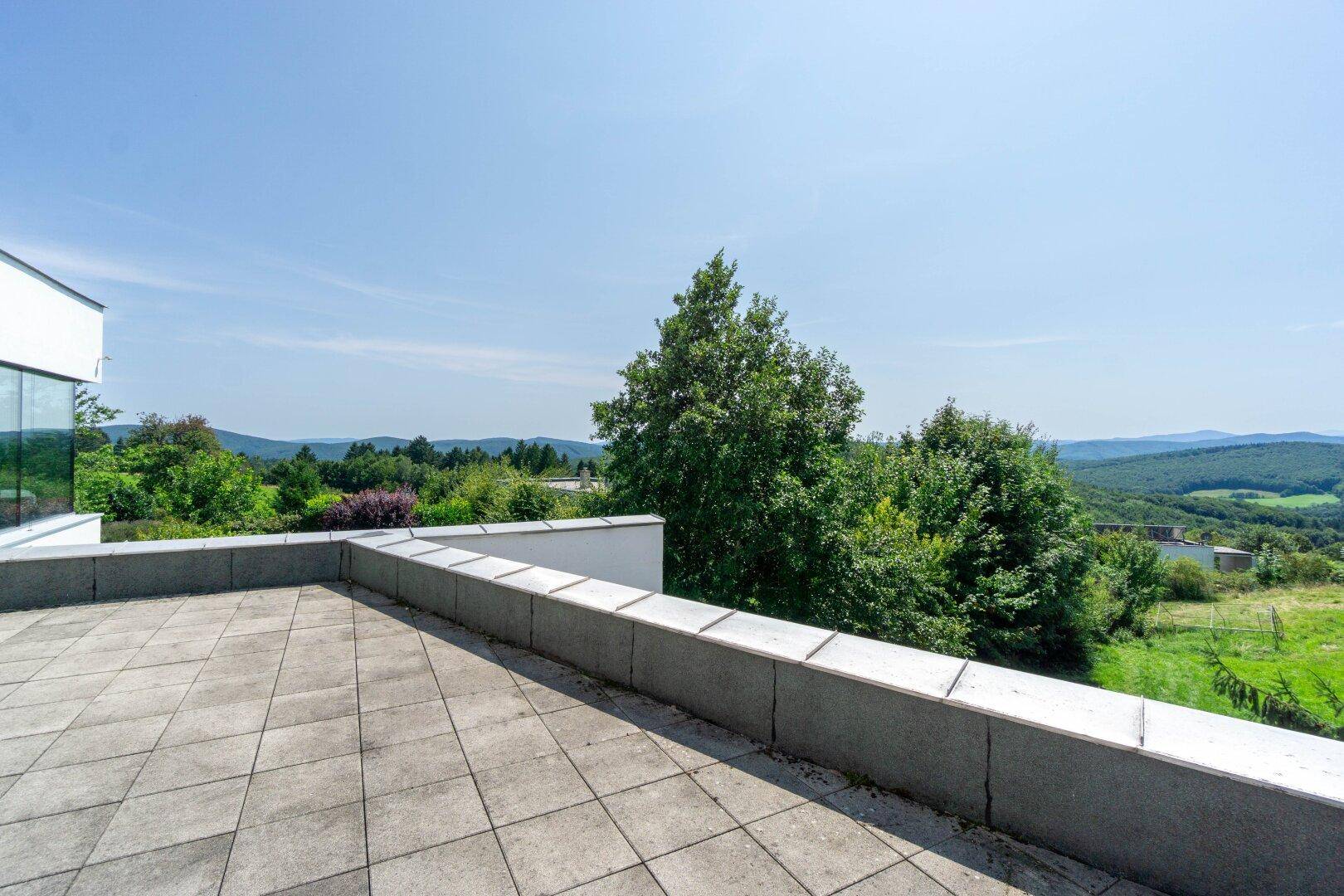Weitläufige Dachterrasse mit Fliesenboden und Panoramablick über die grüne Hügellandschaft.