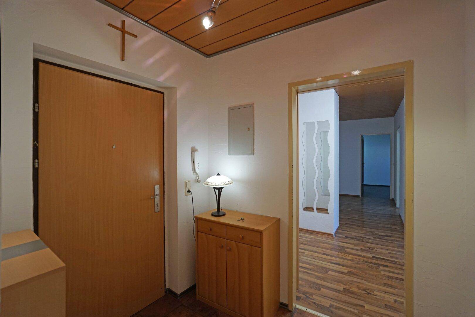 Heller Eingangsbereich mit Holztür, Laminatboden und einer kleinen Kommode.