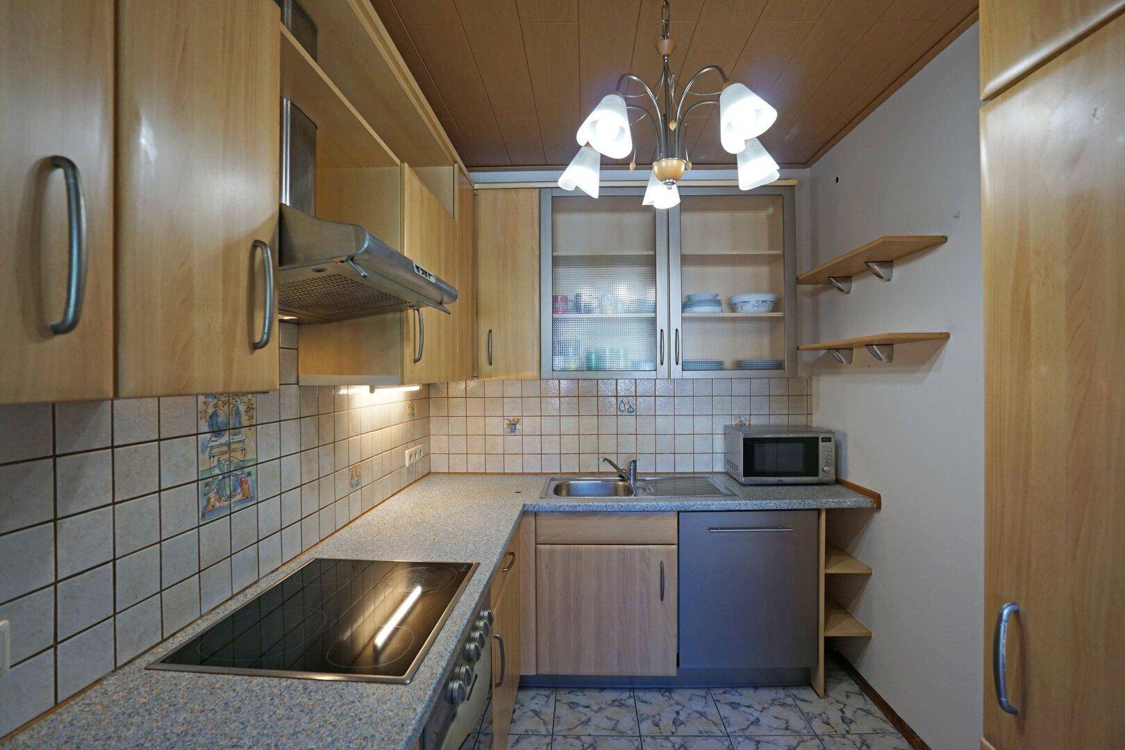 Funktionale Küche mit hellen Holzschränken, Fliesenboden und integrierten Geräten.