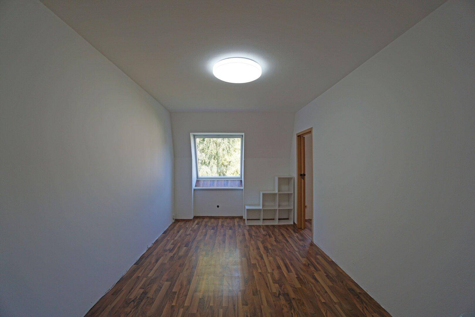 Helles Zimmer mit Laminatboden, weiß gestrichenen Wänden und einem Dachfenster.
