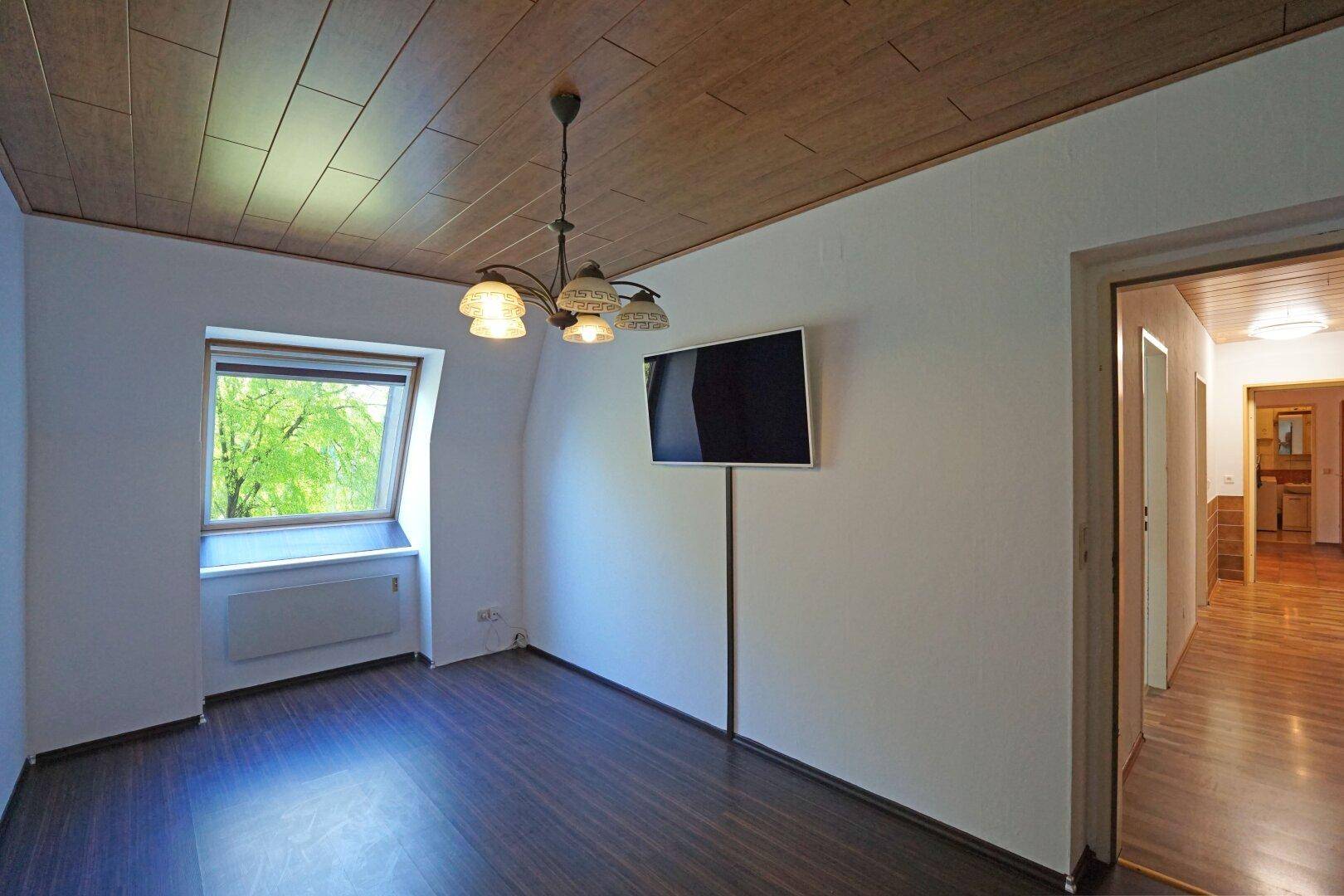 Wohnbereich mit Laminatboden, Holzdecke, Wandfernseher und einem Dachfenster.