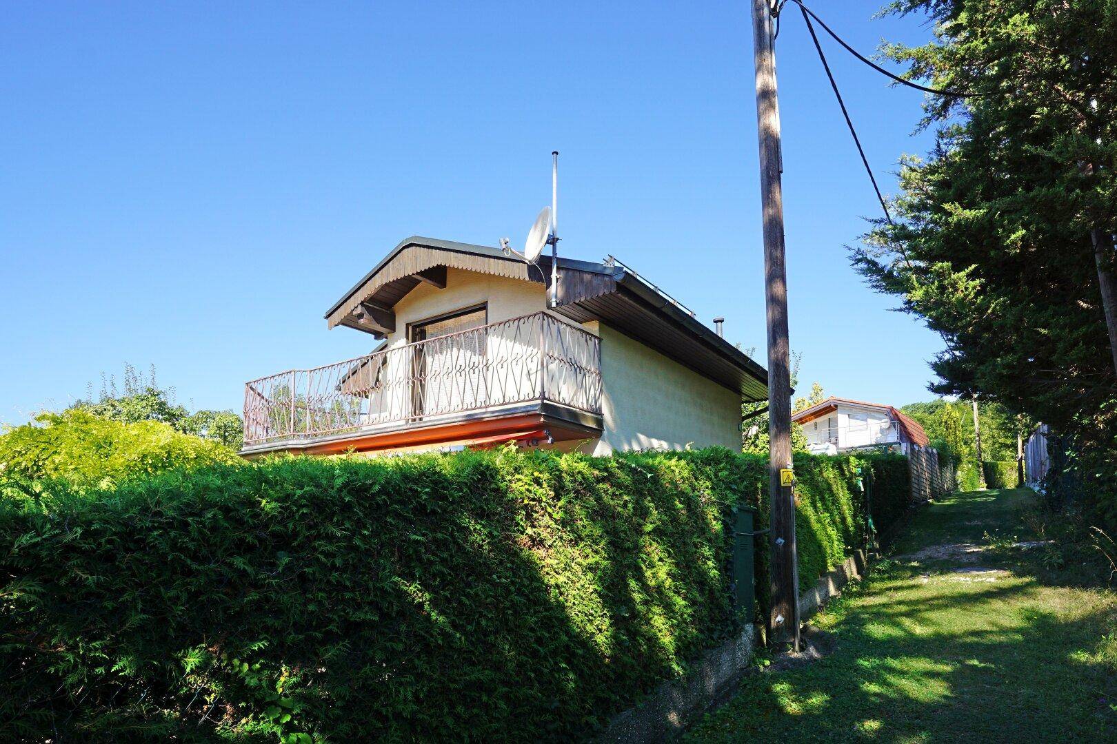 Ansicht des Hauses mit Balkon und umgebender grüner Landschaft unter klarem Himmel.