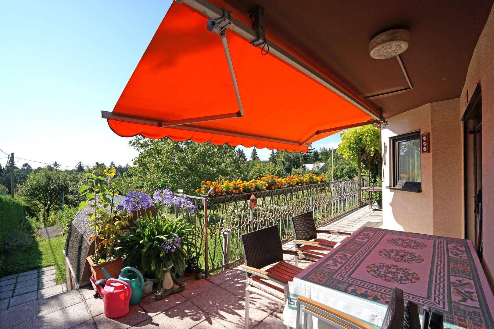 Sonniger Balkon mit Markise, Gartenmöbeln und Blumenkästen mit weitem Blick ins Grüne.