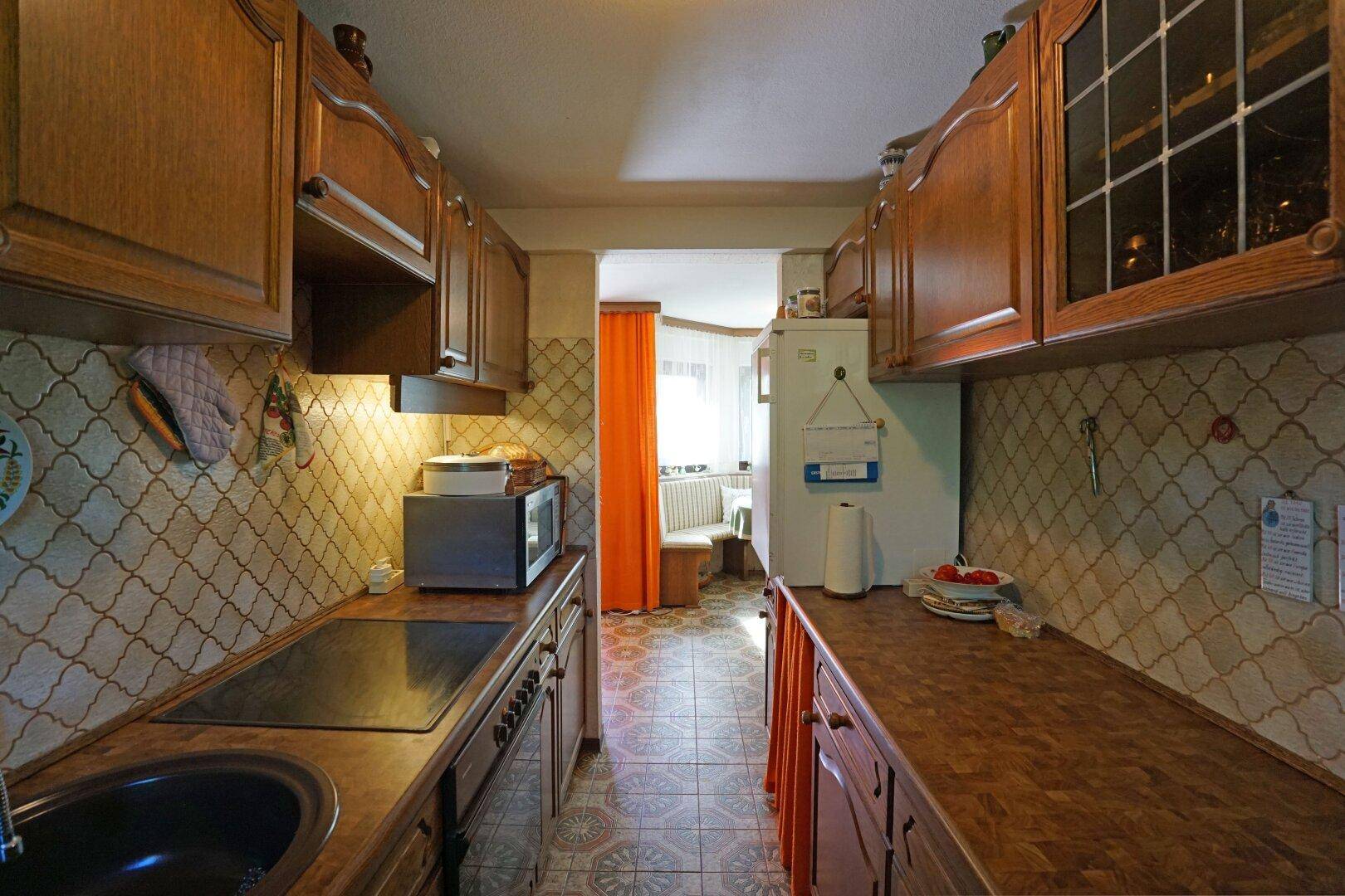 Funktionale Küche mit Holzschränken, Fliesenboden und Blick in einen angrenzenden Essbereich.