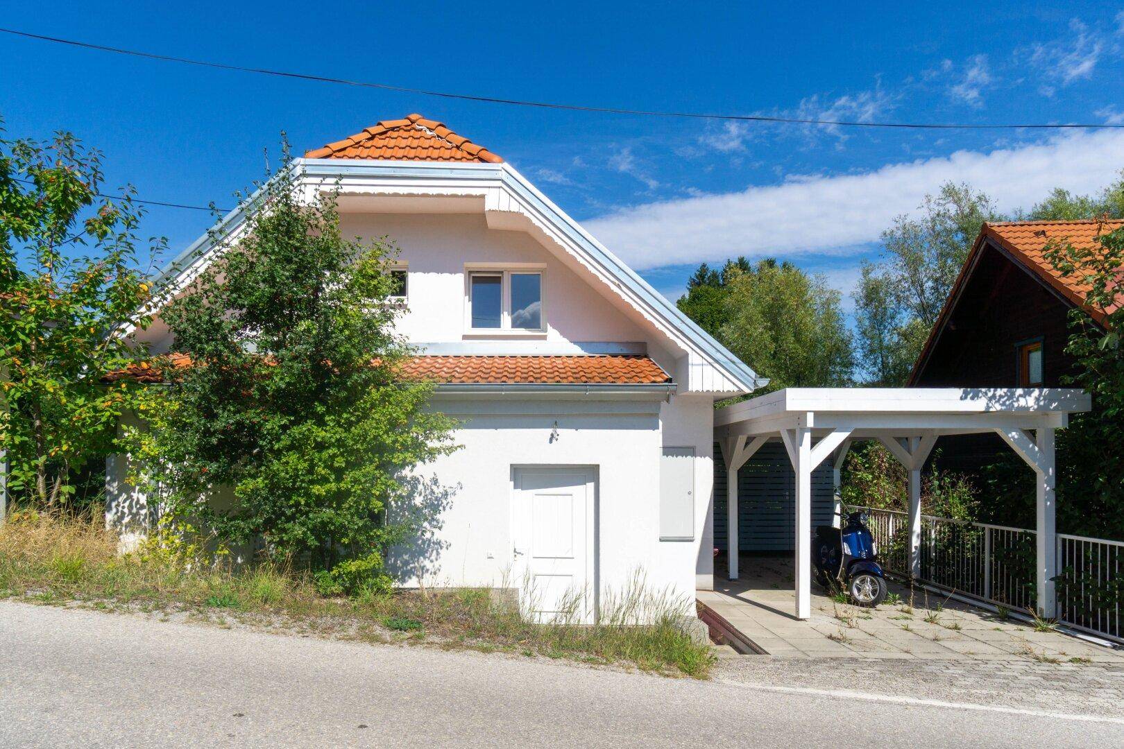 Vorderansicht des Einfamilienhauses mit Carport und Satteldach unter strahlend blauem Himmel.