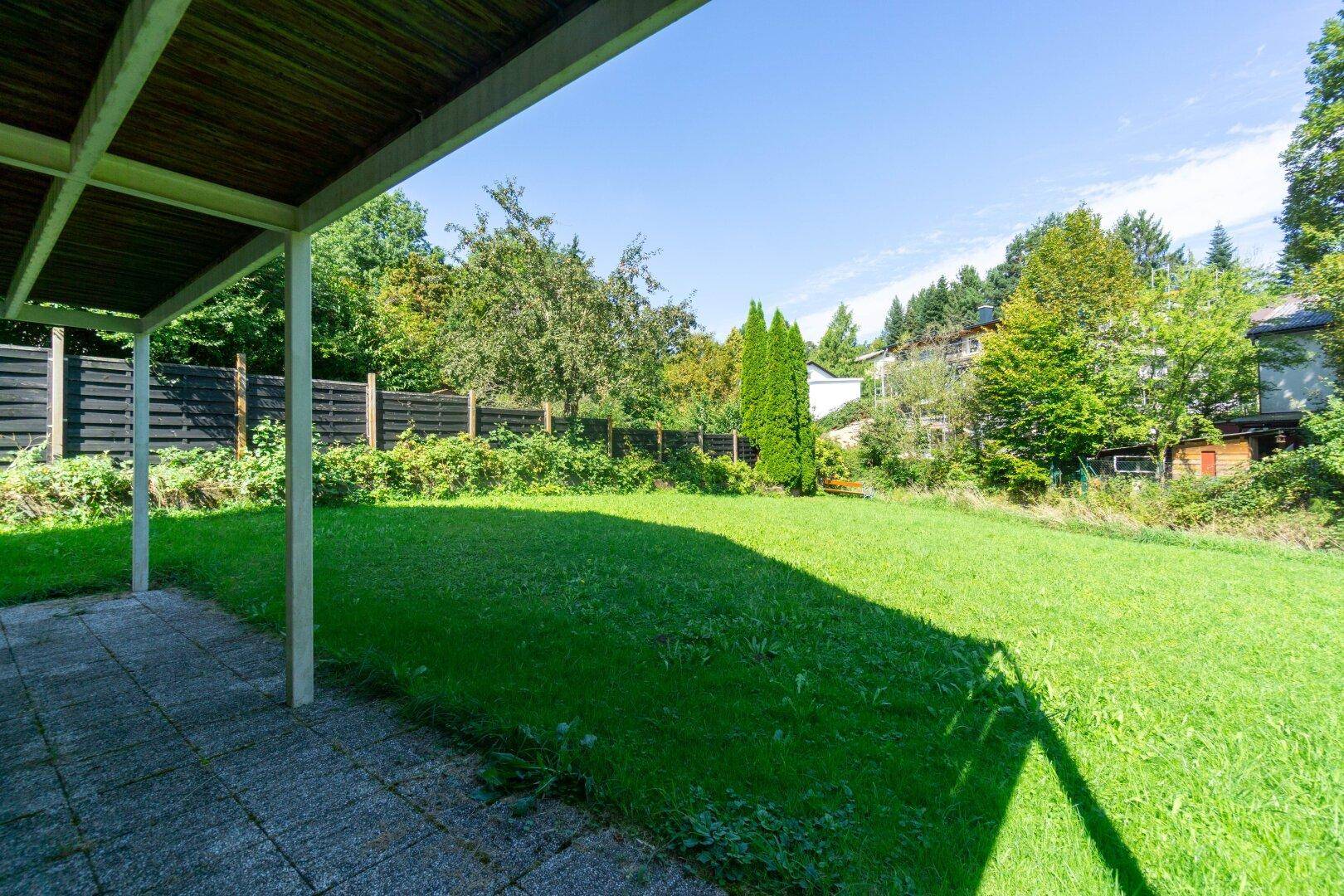 Großer, gepflegter Garten mit Rasenfläche, umgeben von einem Holzzaun und Bäumen.