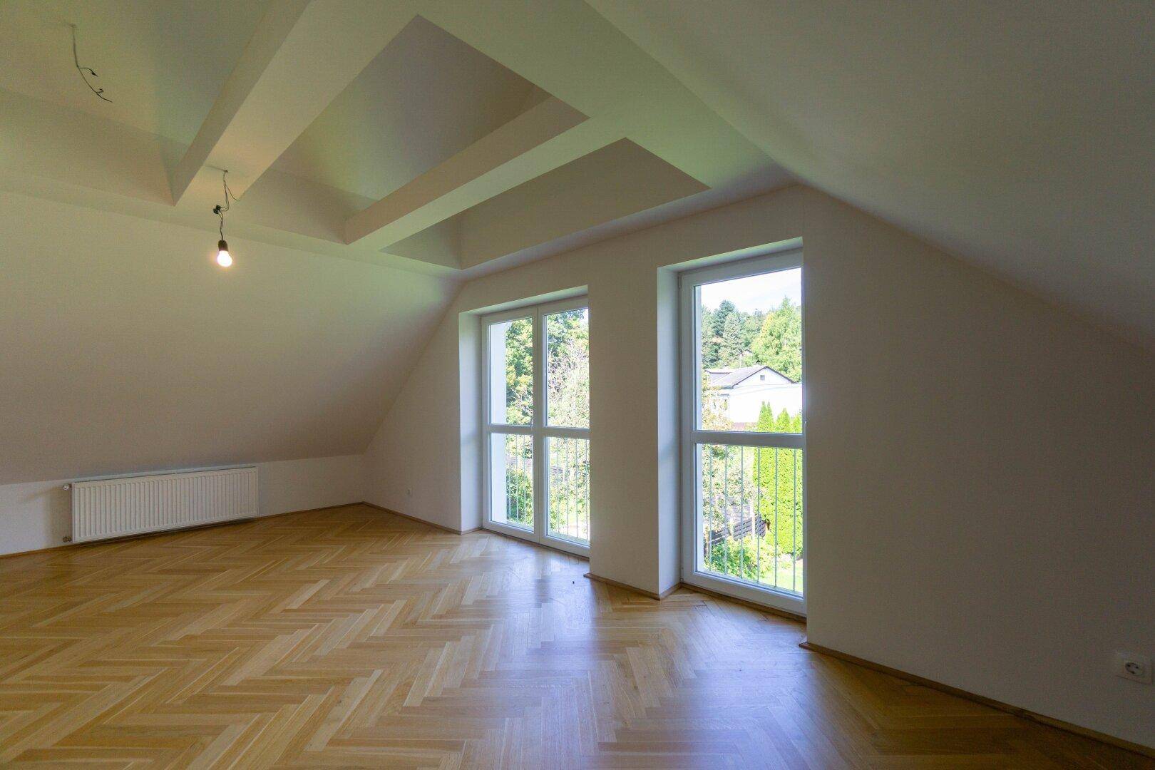 Lichtdurchflutetes Dachgeschosszimmer mit großen Fenstern und Blick ins Grüne.