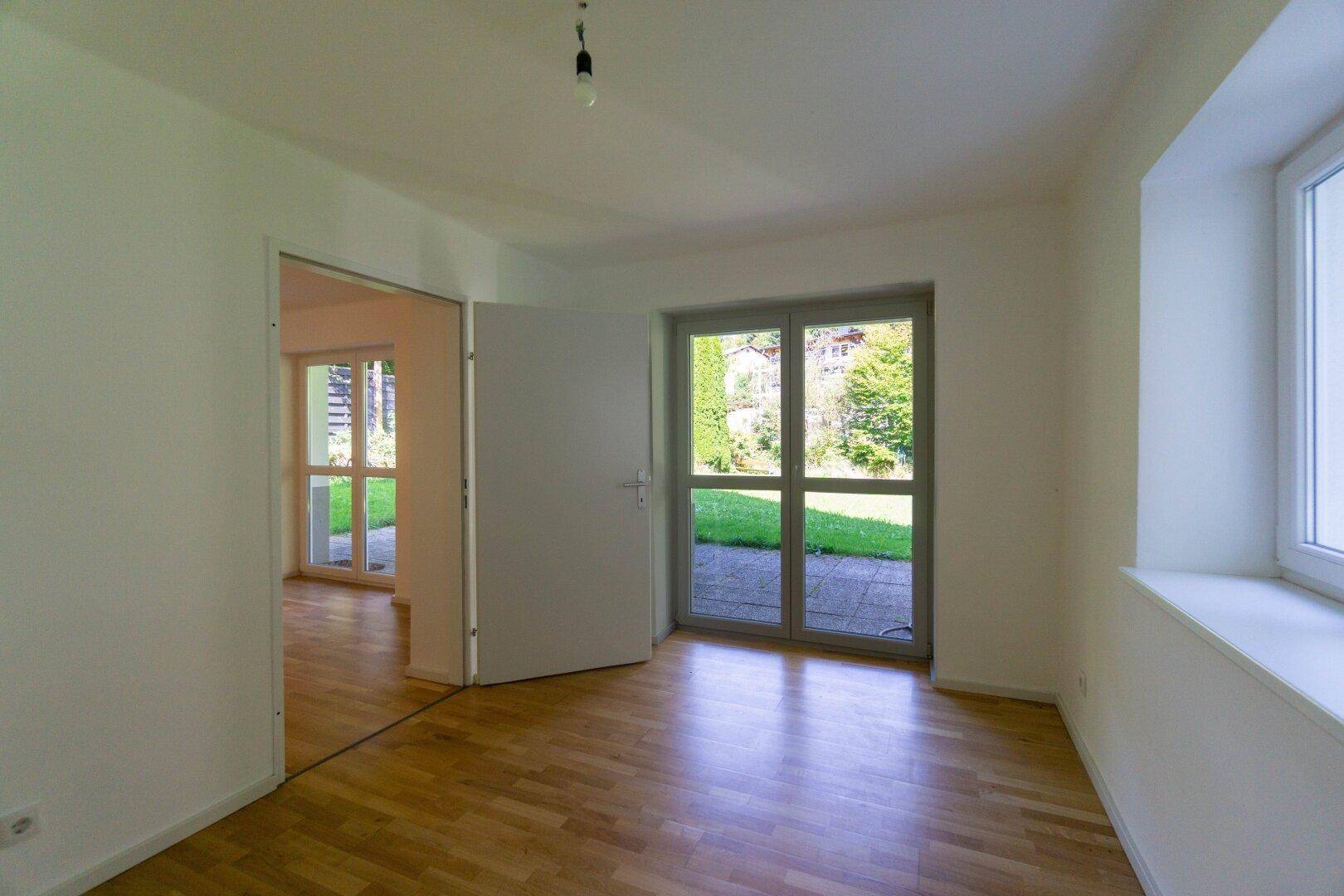 Helles Zimmer mit Parkettboden und Zugang zur Terrasse oder zum Garten, unmöbliert.