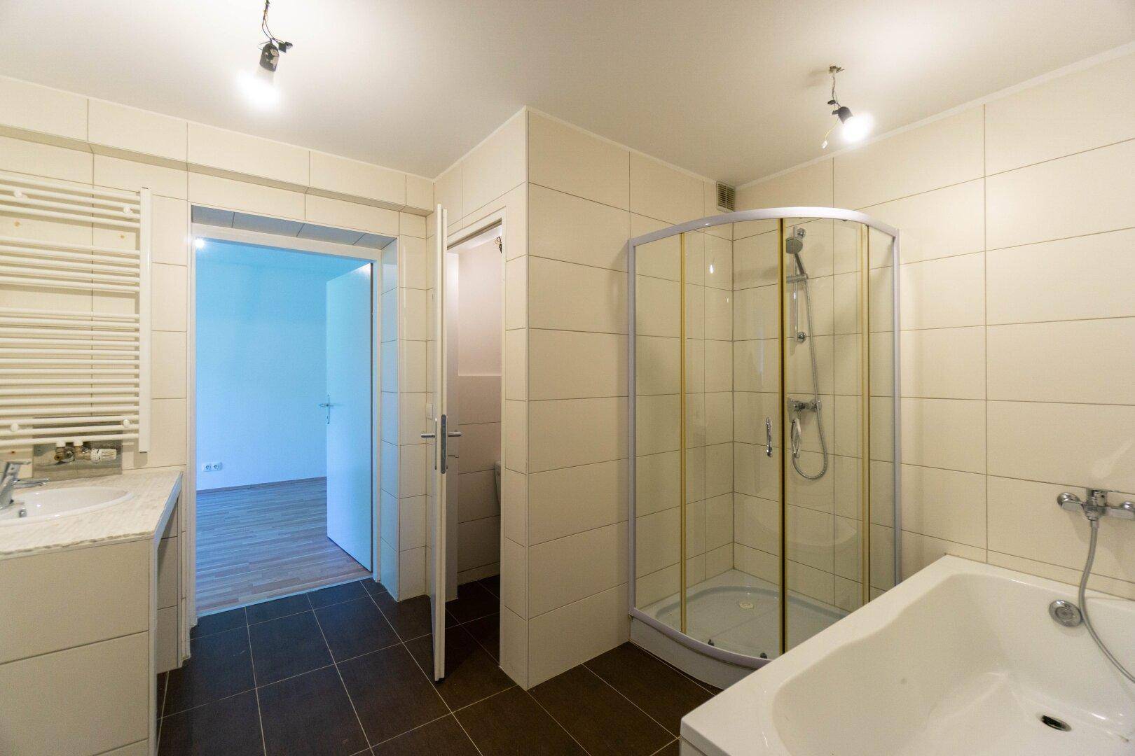 Badezimmer mit Eckdusche, Badewanne, Einzelwaschbecken und Handtuchheizkörper, gefliest.