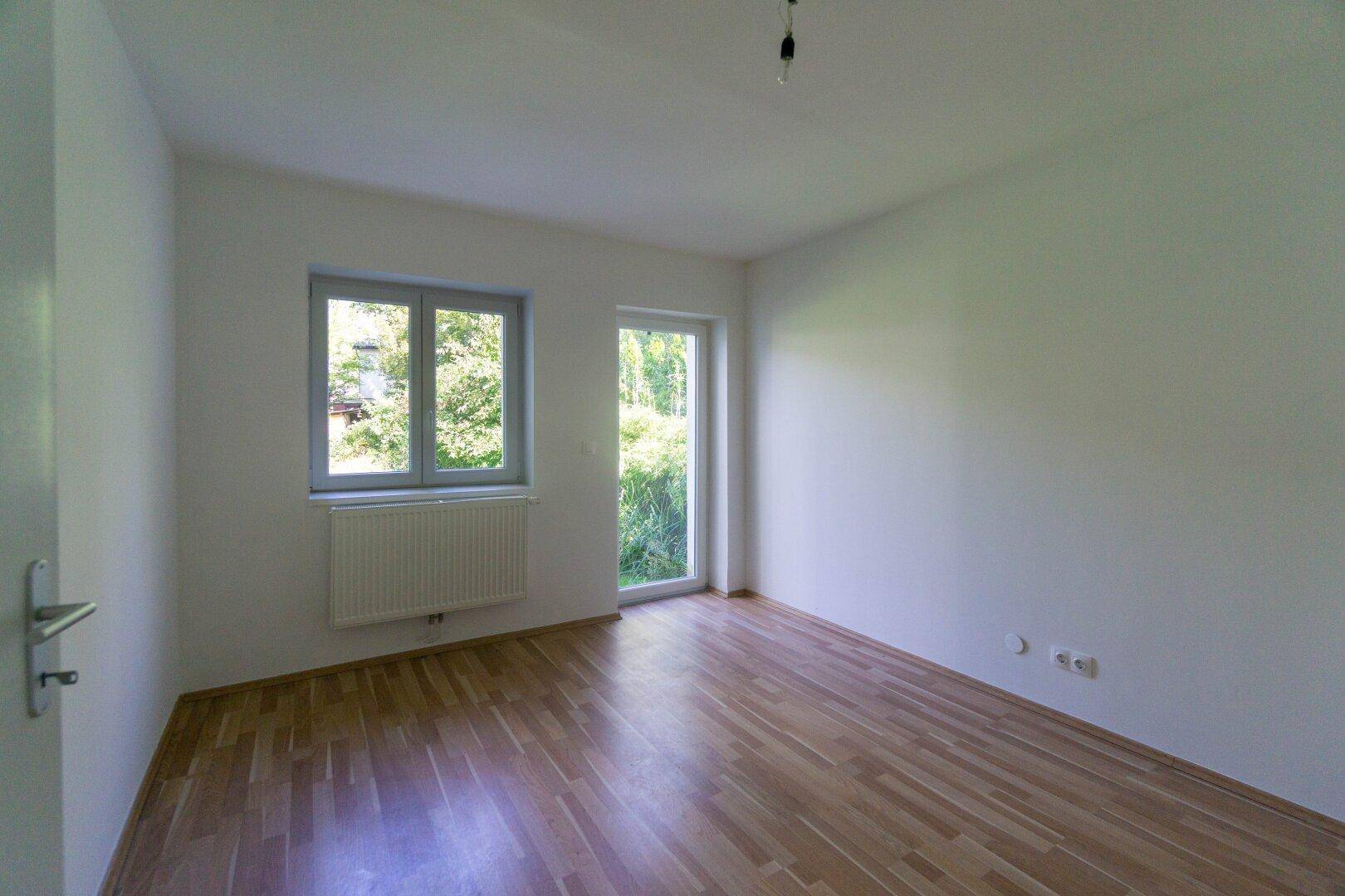 Freundliches Zimmer mit Parkettboden und Fenster mit Blick ins Grüne, unmöbliert.