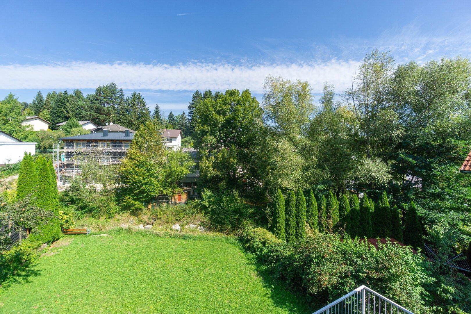 Weitläufiger Blick über den Garten und die grüne Umgebung mit weiteren Häusern und Bäumen.