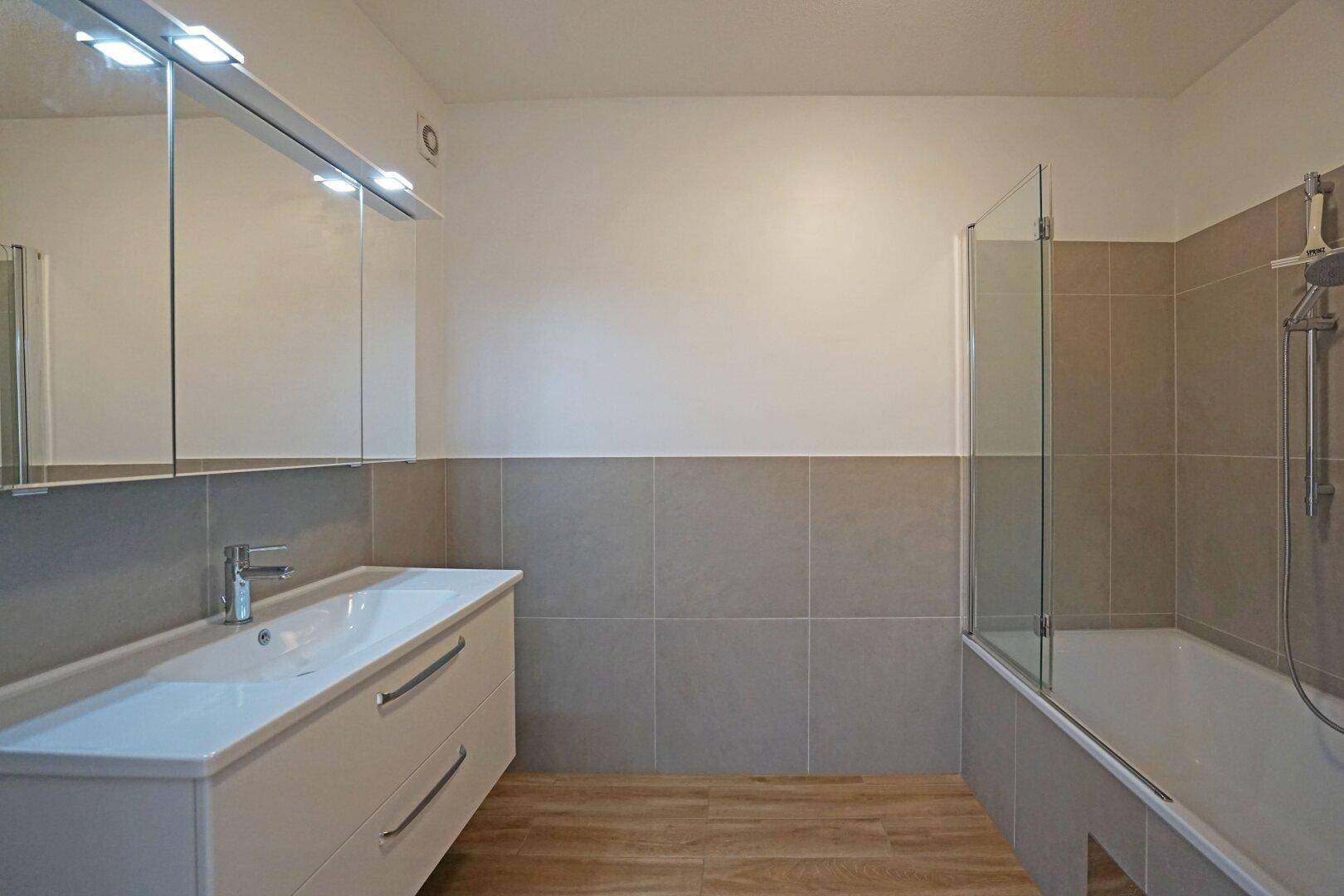 Modernes Badezimmer mit Waschtisch, Spiegelschrank und Badewanne mit Duschabtrennung.